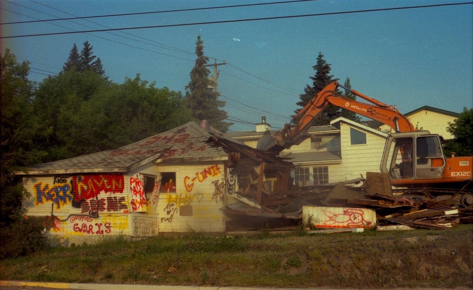 An excavator pulling down the roof and walls of a one-storey house
