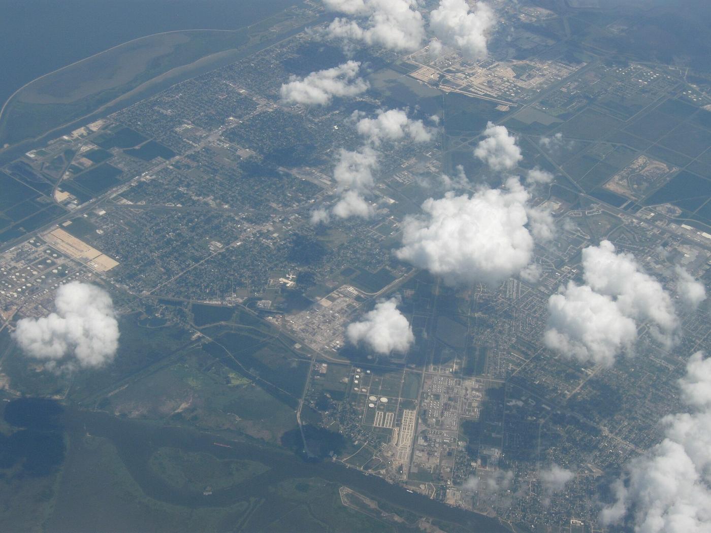 Aerial view of Port Arthur, Texas, with neighborhoods, industrial tank farms and marsh between scattered clouds